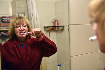 Woman brushing her teeth in a bathroom mirror