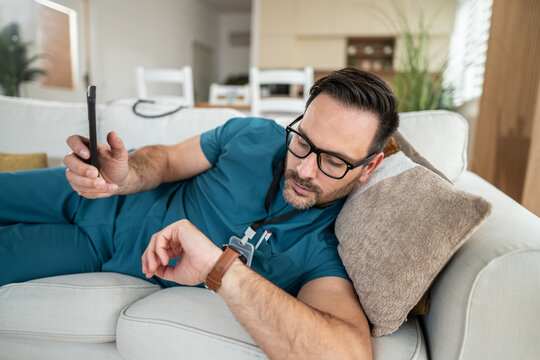 Male doctor resting on couch checking time