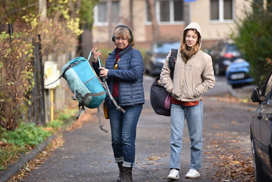 Mother and younf adult daughter walking on a street in autumn with backpacks and headphones