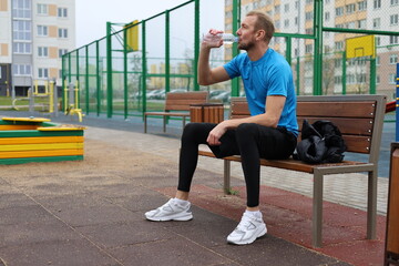 Man taking a hydration break on a sports court bench