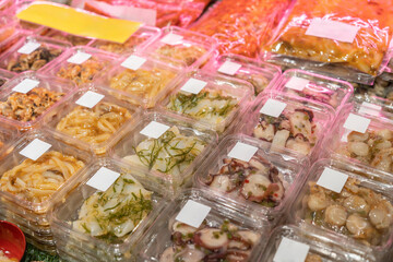 Clear plastic containers filled with different kinds of pre-packaged raw marinated seafood and appetisers selling in the supermarket.