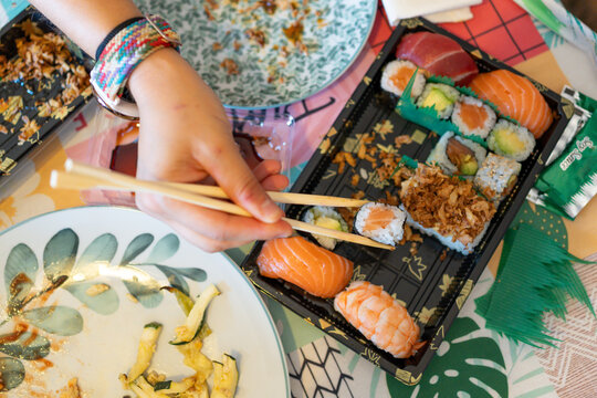 Person eating sushi with chopsticks from takeaway box - Powered by Adobe