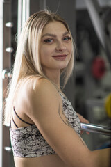 Athletic woman in fitness attire poses confidently in gym, showcasing strength and determination, with exercise equipment and mirrors reflecting her dedication to health and fitness