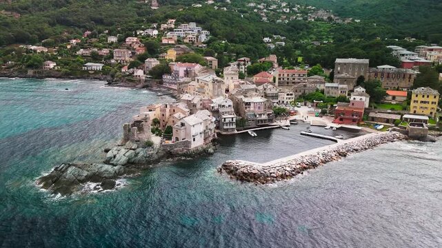 Smooth cinematic aerial drone pan out shot revealing the historic fishing village of Erbalunga, highlighting the ruined Genoese Tower, colorful port, and Mediterranean Sea, Cap Corse, Corsica, France.