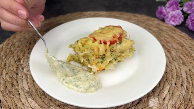 Creamy baked casserole of cabbage pasta and vegetables with cheese and tomato served on white plate with dill sauce