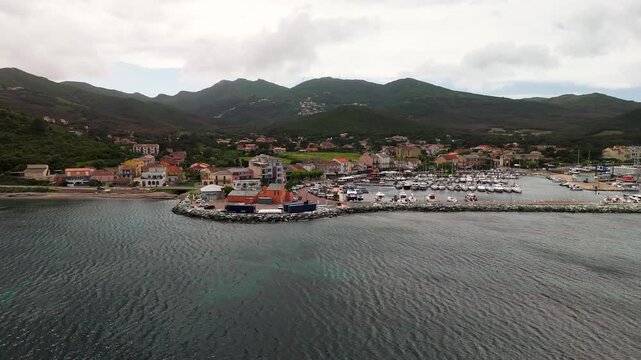 Dynamic Aerial Drone Orbit Circling Macinaggio Village, Harbor, and Marina on the Rugged Coastline of Cap Corse Peninsula, Corsica, France.