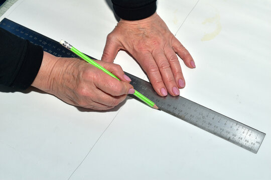 A cutter creates a pattern for fabric. Using a pencil and ruler, he draws the pattern pieces.