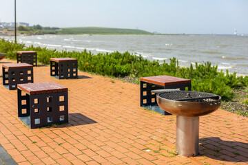 Sunny summer day at Sillamae beach promenade (Estonian - Sillam&auml;e), Estonia. Modern brick-paved area with steel barbecue grill and wooden benches by the Baltic Sea. 
