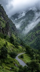 Obraz premium Winding road through lush green mountains shrouded in mist and low-hanging clouds.