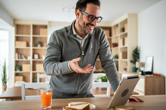 Man having video call on tablet from home while eating breakfast - Powered by Adobe