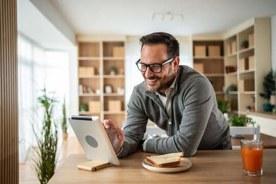 Man with tablet having breakfast at home smiling