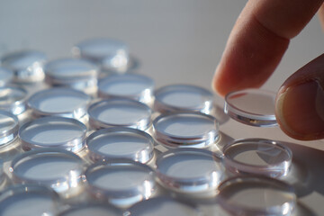 Numerous Clear Glass Discs Arrayed with Finger Carefully Picking One Depicts Precision and Focus in Transparent Material Manipulation