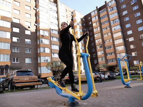 Young woman actively exercising on outdoor fitness equipment in a city park or residential area. Concept of healthy lifestyle, urban wellness, and accessible sport activities. - Powered by Adobe