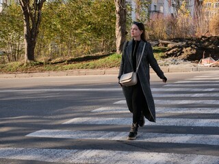 Fototapeta premium Stylish woman walking actively on a city street or sidewalk. Concept of urban lifestyle, daily commute, leisure time, and dynamic movement in a metropolitan area.