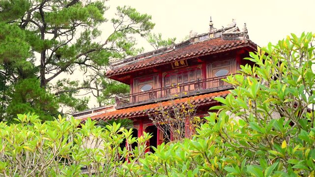 Minh Lau Pavilion viewed across a stone bridge, surrounded by lush gardens and pines at Minh Mang Tomb.