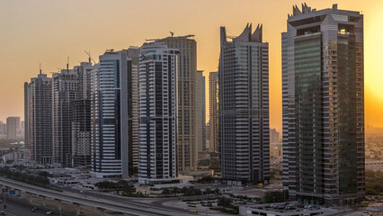 Naklejka premium Aerial view of Jumeirah lakes towers skyscrapers night to day timelapse with traffic on sheikh zayed road.