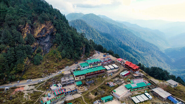 Aerial drone village town on cliff mountain edge with small concrete green red houses, narrow road and mountains in the distance in Chopta Tungnath uttarakhand India