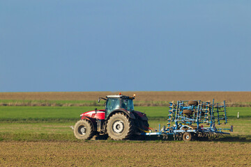 Obraz premium Red tractor pulling a cultivator in an agricultural field