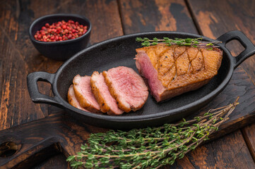 Seared duck breast sliced and served in cast-iron skillet with thyme on rustic wooden background ideal for gourmet food photography.