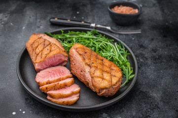 Gourmet grilled duck fillet with crispy skin and tender slices served on black plate over textured dark surface ideal for food photography.