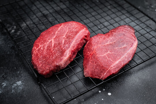 Marbled Wagyu beef chuck steaks similar to angus and yakiniku cuts placed on grill rack with pepper bowl on dark stone backdrop great for butcher photography.