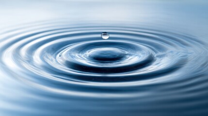 A single water droplet falls onto a smooth blue surface creating soft ripples that spread outward. This moment captures the peaceful interplay of water and beauty in nature.