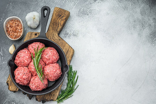 Uncooked raw meatballs Polpette style with garlic and salt in black skillet highlighting raw texture perfect for culinary and butcher visuals. - Powered by Adobe