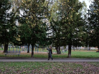 Fototapeta premium Woman enjoying a walk in the park while having a video call on her smartphone. Concept of outdoor leisure, modern connectivity, remote communication, and balancing nature and technology.