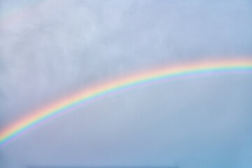 Vibrant rainbow arching through soft cloudy sky