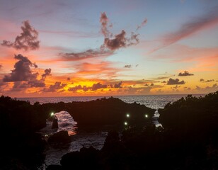 Fototapeta premium Breathtaking scenic view of a fiery sunset over the ocean with a silhouetted natural rock arch bridge