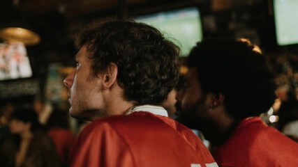 Fans in red shirts cheer at glowing screens in a lively bar environment expressing team loyalty competitive spirit and emotional live sports culture