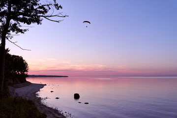 Tranquil Baltic Sea coastline at sunset with paraglider in sky