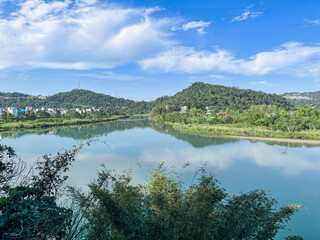 Tranquil afternoon scene of Qingtan Weir with mirror-like turquoise water reflecting blue sky and lush mountains in Xindian District, New Taipei City, Taiwan.