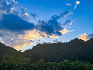 Stunning dawn sky with dramatic orange and golden clouds over the lush forested mountains of Wulai, New Taipei City, Taiwan. Early morning light illuminates the valley and river below.