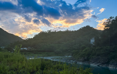 Stunning dawn scenery in Wulai, New Taipei City, Taiwan. Golden clouds illuminate the sky above mountain valleys and a peaceful river with rocky shores.