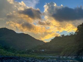 Scenic morning landscape of the Nanshi River in Wulai, New Taipei City, Taiwan, featuring vibrant orange and yellow clouds above the lush green mountains at sunrise.