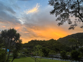 Vivid orange and yellow sunrise sky above the lush green mountains and river area in Wulai, New Taipei City, Taiwan, seen from a park or open space.