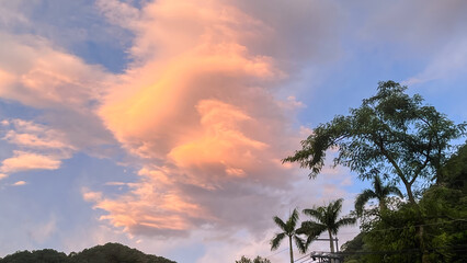 Close up view of vibrant pink and orange clouds in the dawn sky above the silhouette of palm trees and mountains in Wulai, New Taipei City, Taiwan.
