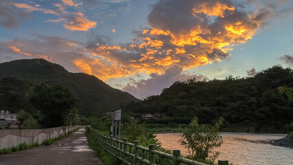 Spectacular sunrise with dramatic orange and golden clouds illuminating the dark silhouette of Wulai mountains in New Taipei City Taiwan at dawn.