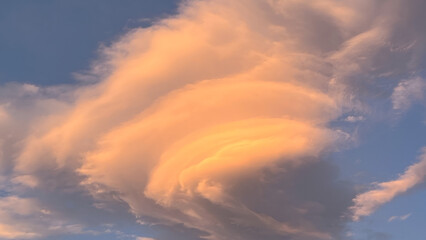 The beauty of a unique lenticular cloud formation against a blue sky. Cloud layers are illuminated with warm orange and pink sunlight during dawn in Wulai Taiwan.