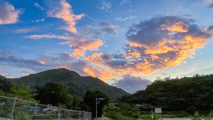 Dramatic sunrise or sunset sky over the silhouette of forested mountains and lush greenery in Wulai New Taipei City Taiwan. Clouds are brightly lit in orange and gold.
