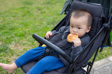 Baby sitting on stroller eating bread at park