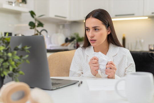 Young woman at home crumples wrong bill throws page beside laptop plans to print new fixed copy. Caucasian girl on sofa sits at table looks upset prepares fresh invoice checks amount types again calm.