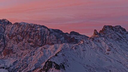 Aerial footage of the snowy mountain peaks of Val Gardena, Italy, as the first sunrise light paints the sky in soft pink and violet tones. Captured in cinematic 4K. - Powered by Adobe