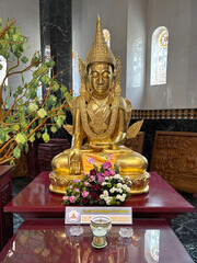 Golden Kakusandha Buddha statue inside Kek Lok Si Temple, Penang, Malaysia. Ornate Buddhist figure on a red altar with offerings. Symbolizes the first Buddha of the Bhadrakalpa.