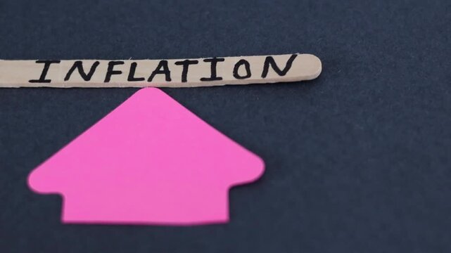 Un primer plano de una paleta de madera con la palabra de inflaci&oacute;n y una flecha con movimiento en un fondo gris oscuro. Pol&iacute;tica econ&oacute;mica 