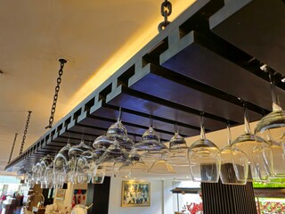 Hanging wine glasses arranged upside down on a bar rack in a modern restaurant interior with stylish lighting and reflective glass details.