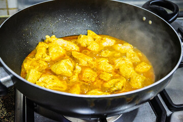 cooking chicken in curry with steam on a home stove