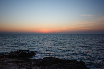 Serene ocean view at sunset, with gentle waves lapping against rocky shore, creating a tranquil atmosphere and showcasing the beauty of nature's evening colors