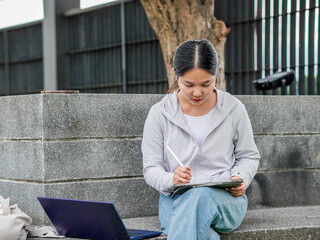 Businesswoman using phone and laptop remote work at park for AI chat bot, goal planning browsing internet. Young professionals freelance digital transformation. Female leadership new beginnings 